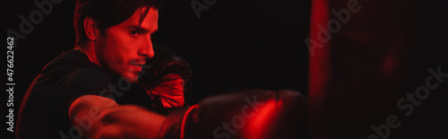 Sportsman in boxing gloves working out with blurred punching bag isolated on black, banner photo