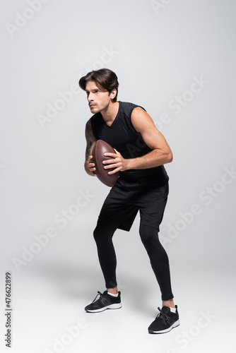 Full length of rugby player holding ball on grey background