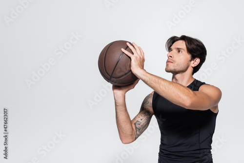Sportsman holding basketball ball while looking away isolated on grey © LIGHTFIELD STUDIOS