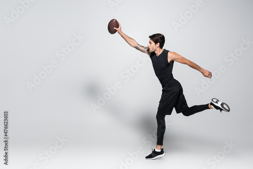 Side view of player with rugby ball running on grey background © LIGHTFIELD STUDIOS