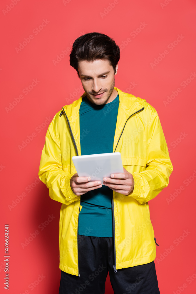 Sportsman in yellow sports jacket using digital tablet on red background Sportsman in yellow sports jacket using digital tablet on red background