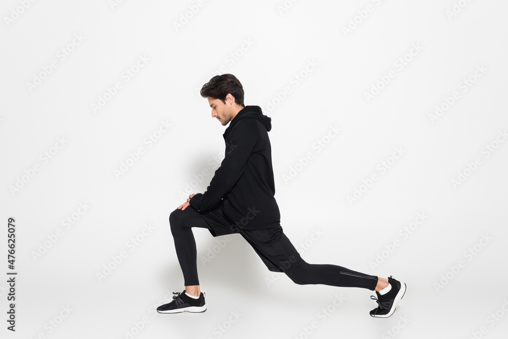 Side view of sportsman in sports jacket doing lunges on grey background Side view of sportsman in sports jacket doing lunges on grey background