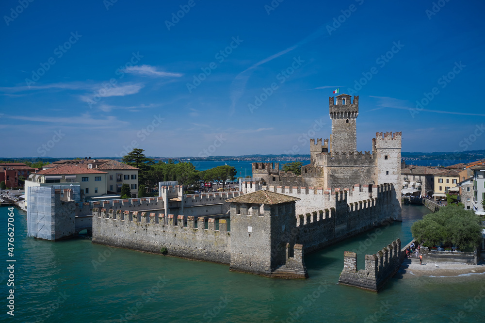 Italian castles Scaligero on the water. Flag of Italy on the towers of the castle on Lake Garda. Top view of the 13th century castle. Aerial panorama of Sirmione castle, Lake Garda, Italy.