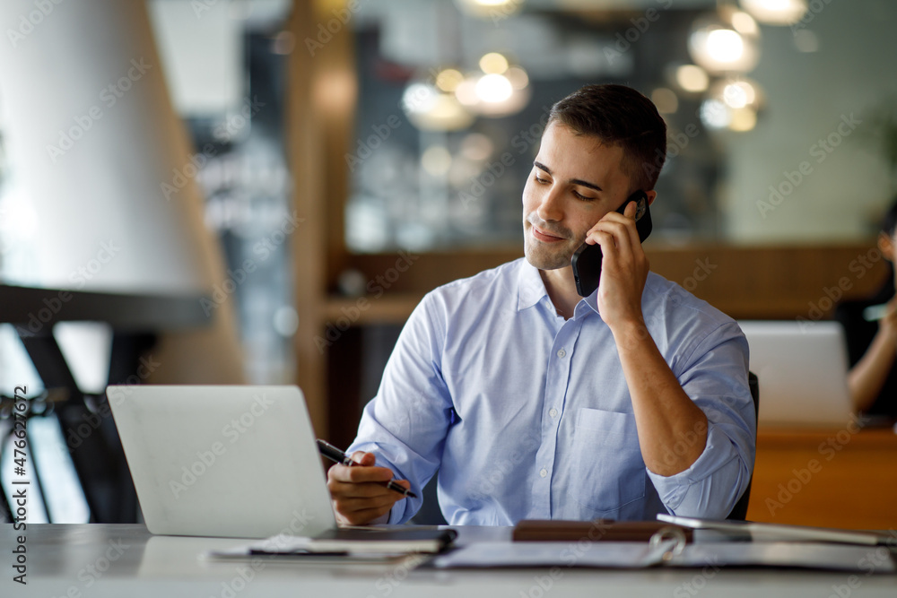 Smiling businessman dressed in white shirt sitting in the office and using tablet computer while talking by his phone. Smiling businessman dressed in white shirt sitting in the office and using tablet computer while talking by his phone.