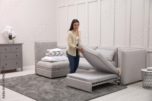 Woman making sleeping place for guest in living room. Convertible sofa