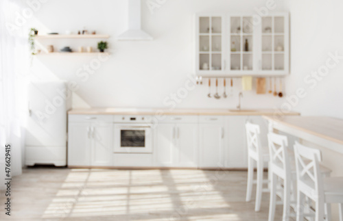 Blurred light sunny kitchen in Scandinavian style. White kitchen furniture and dining area, copy space