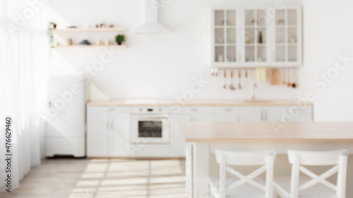 Sunny kitchen interior in Scandinavian style with white kitchen furniture and dining area, blurred background © Prostock-studio