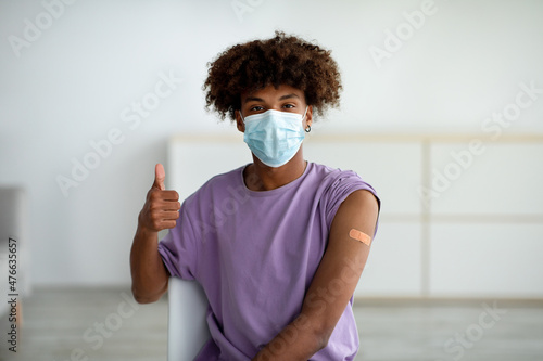 Foto Black teen guy in face mask wearing plaster bandage on his arm after covid vacci