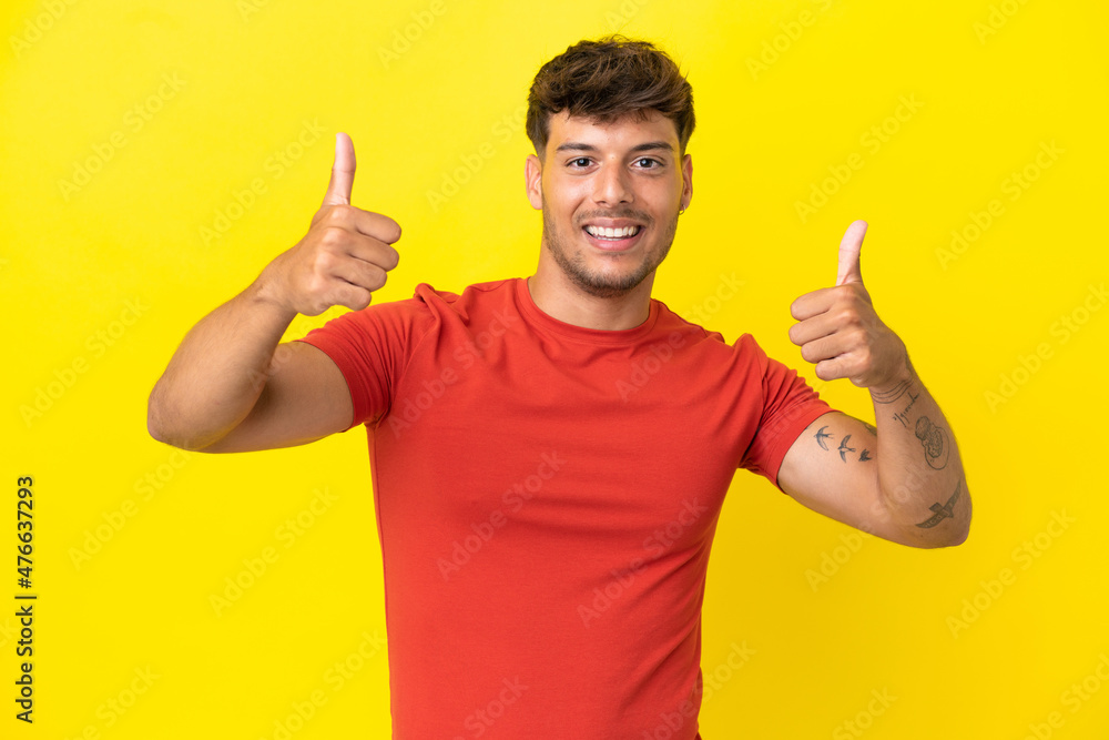 Young caucasian handsome man isolated on yellow background giving a thumbs up gesture Young caucasian handsome man isolated on yellow background giving a thumbs up gesture