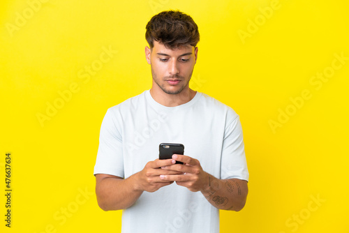 Young caucasian handsome man isolated on yellow background using mobile phone © luismolinero