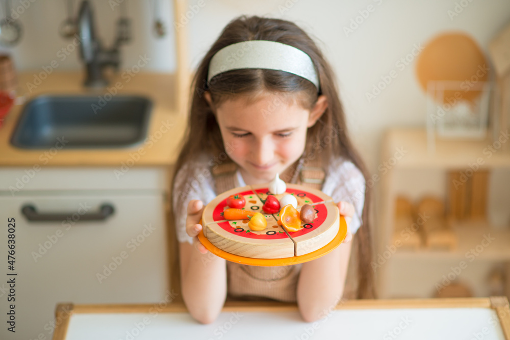 little girl plays in the children's kitchen. toy pizza. scandinavian children's room