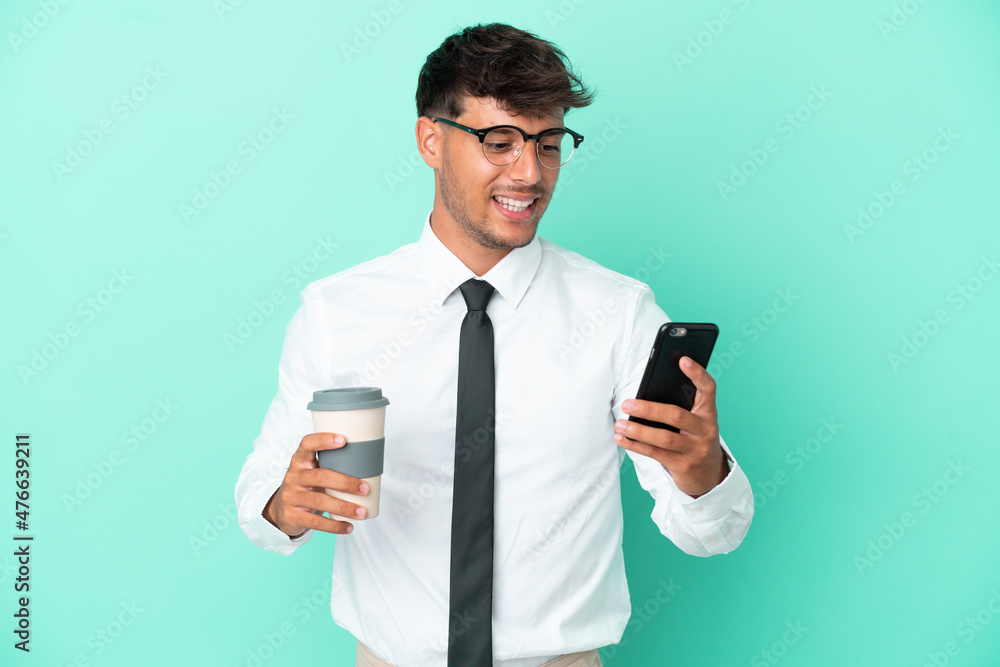 Business caucasian man isolated on blue background holding coffee to take away and a mobile Business caucasian man isolated on blue background holding coffee to take away and a mobile