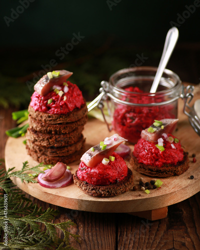 Russian cuisine. A festive dish. Snack with beetroot and herring. Herring salad under a fur coat with bread. Salad of boiled beetroot, vegetables with green onions and dill on a wooden board. Rustic