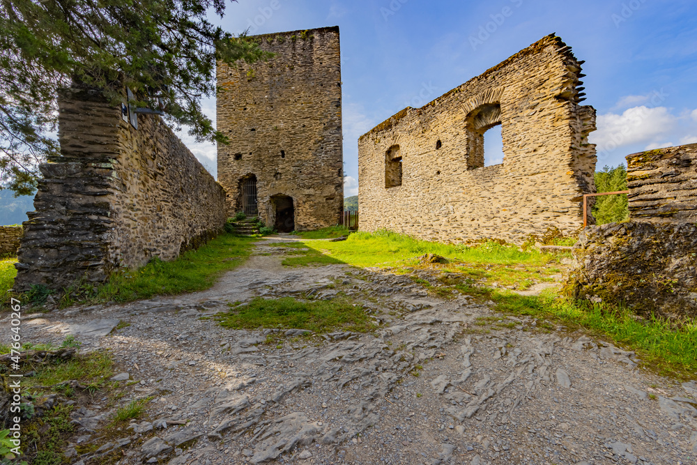 Ruins of the castle of Esch-sur-Sure with a broken stone fence, wall with square windows and a square tower in the background, green grass, sunny summer day with a blue sky in Luxembourg Ruins of the castle of Esch-sur-Sure with a broken stone fence, wall with square windows and a square tower in the background, green grass, sunny summer day with a blue sky in Luxembourg