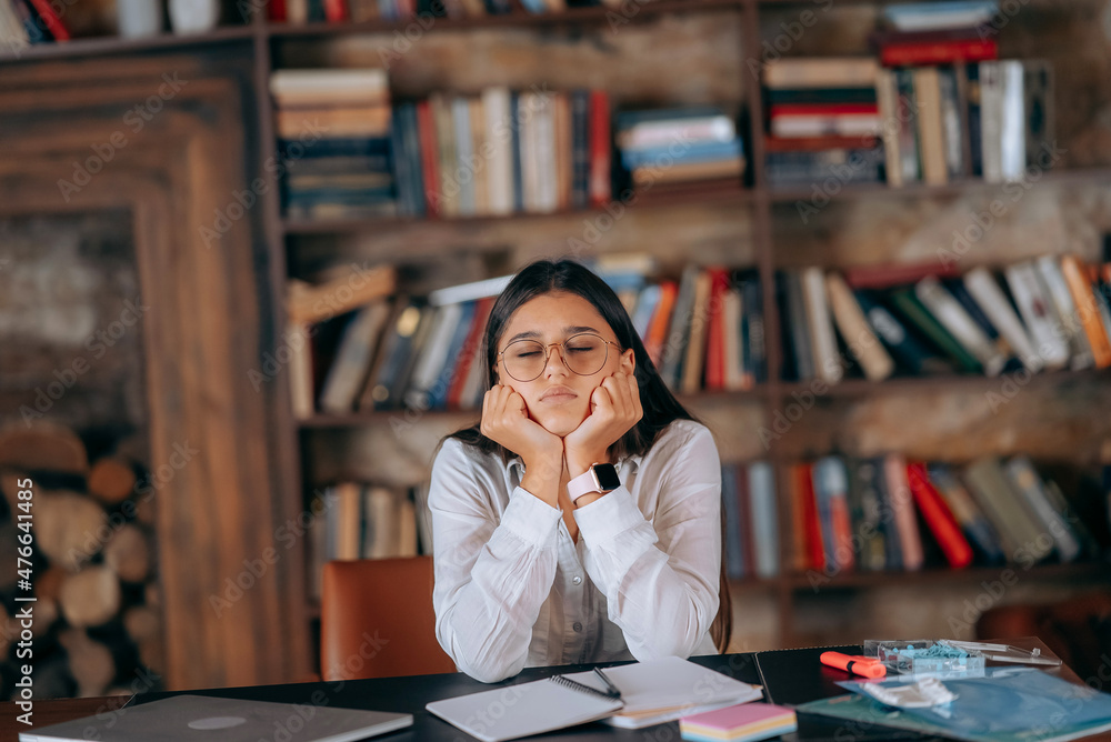 Young woman in office thinking over problem on background of bookshelves Young woman in office thinking over problem on background of bookshelves