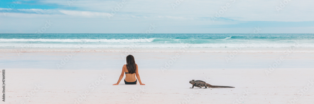 Beach vacation funny marine iguana walking by woman tanning on