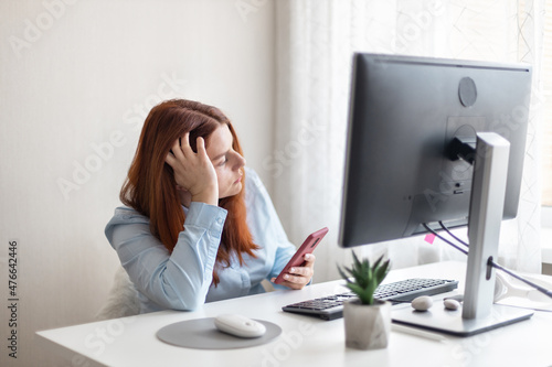 Fotografie Tired woman stressed by a lot of work, sitting at the desk and using smartphone