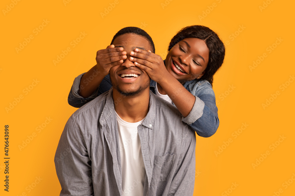 Fototapeta premium Happy african woman surprising her excited boyfriend, covering his eyes