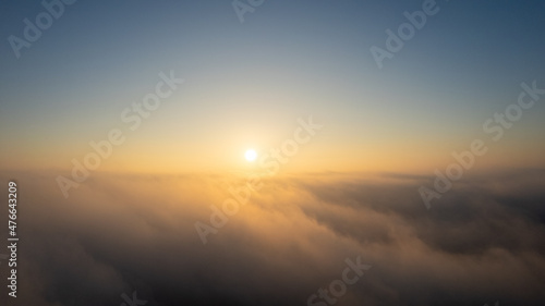 Aerial View. Flying in fog  fly in mist over the early morning clouds in the rising sun. Aerial camera shot. Flight above the clouds towards the sun with the mist clouds floating by. Misty weather