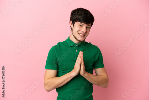 Young Russian man isolated on pink background keeps palm together. Person asks for something