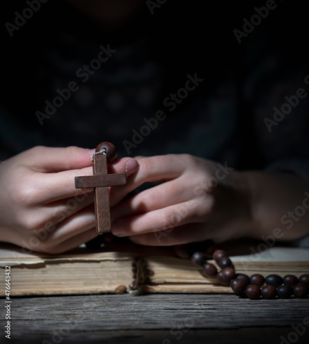 Young beautiful girl praying to God with wooden rosary. Close up.