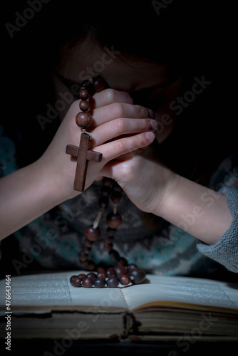 Young beautiful girl praying to God with wooden rosary. Vertical image.