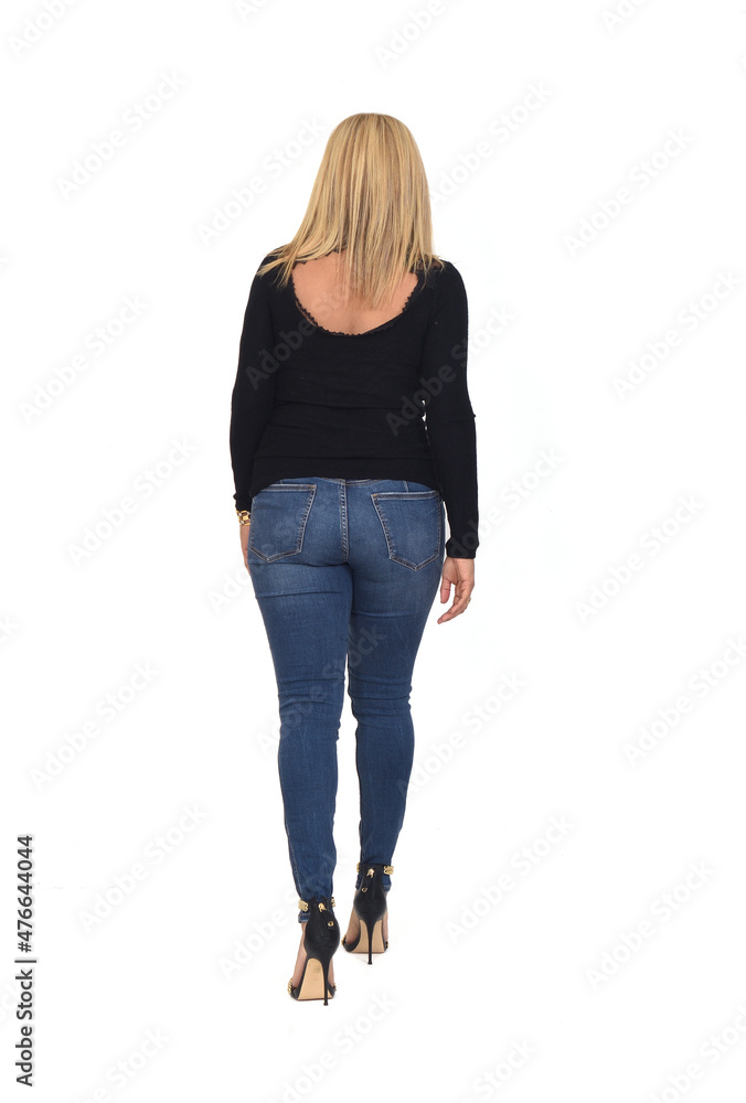 rear view of  blonde woman walking with jeans and heeled shoes on white background