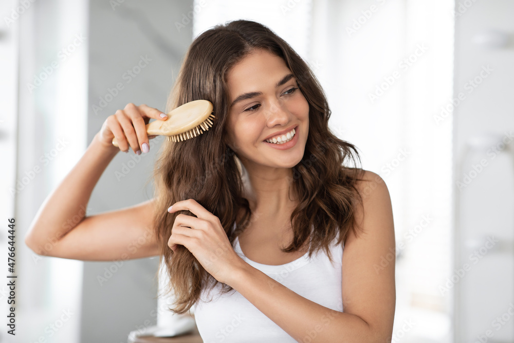 Happy Young Female Brushing Hair With Brush Standing In Bathroom Stock