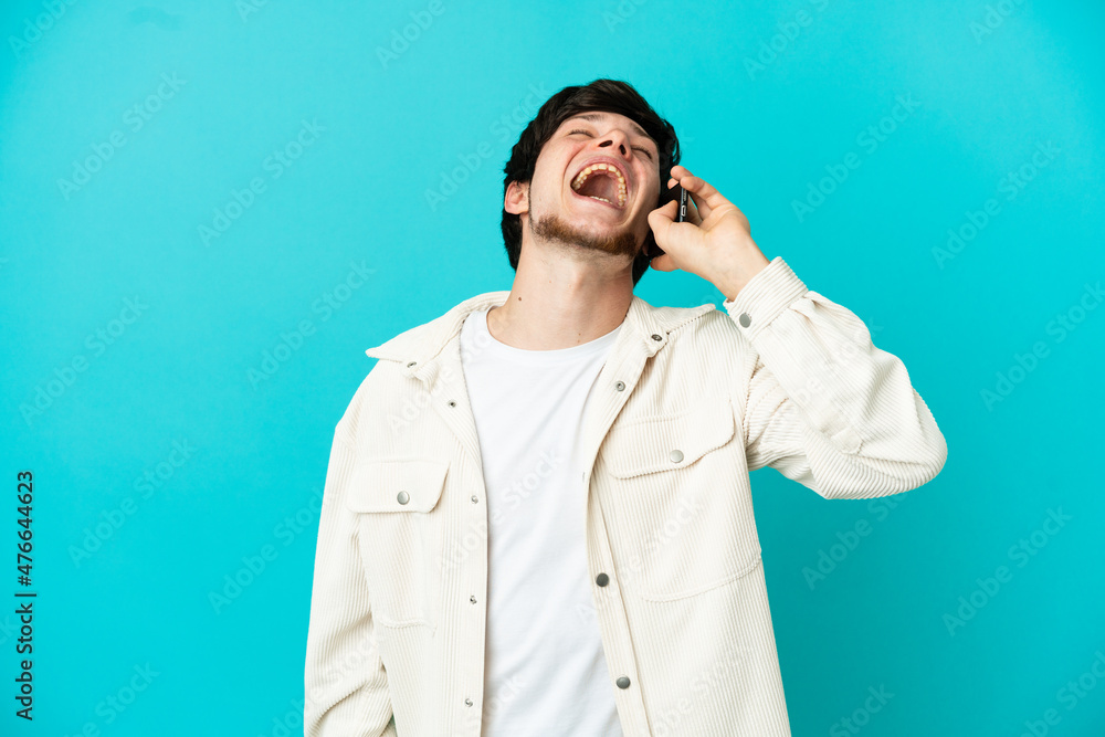 Young Russian man using mobile phone isolated on blue background laughing Young Russian man using mobile phone isolated on blue background laughing