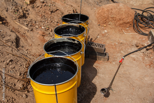 Bitumen mastic in buckets. Protective bitumen mastic for concrete pavement. Material for waterproofing the foundation.