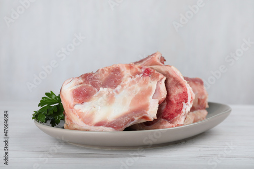 Plate with raw chopped meaty bones and parsley on white wooden table