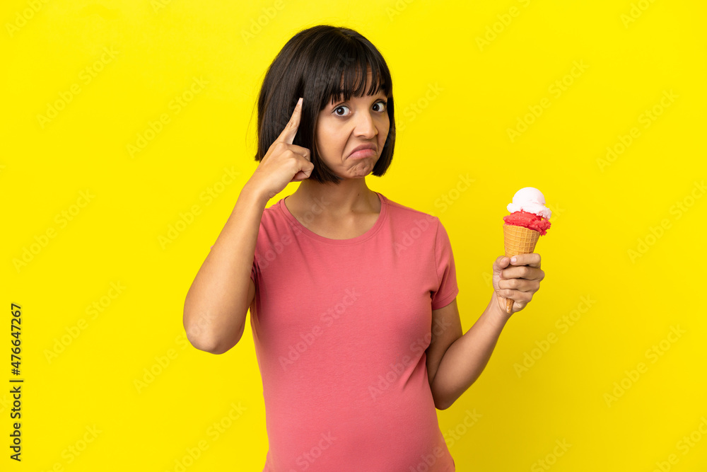 Pregnant woman holding a cornet ice cream isolated on yellow background thinking an idea Pregnant woman holding a cornet ice cream isolated on yellow background thinking an idea