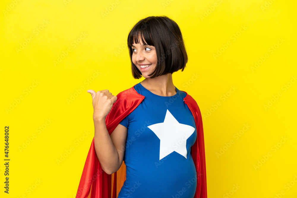 Super Hero pregnant woman isolated on yellow background pointing to the side to present a product Super Hero pregnant woman isolated on yellow background pointing to the side to present a product