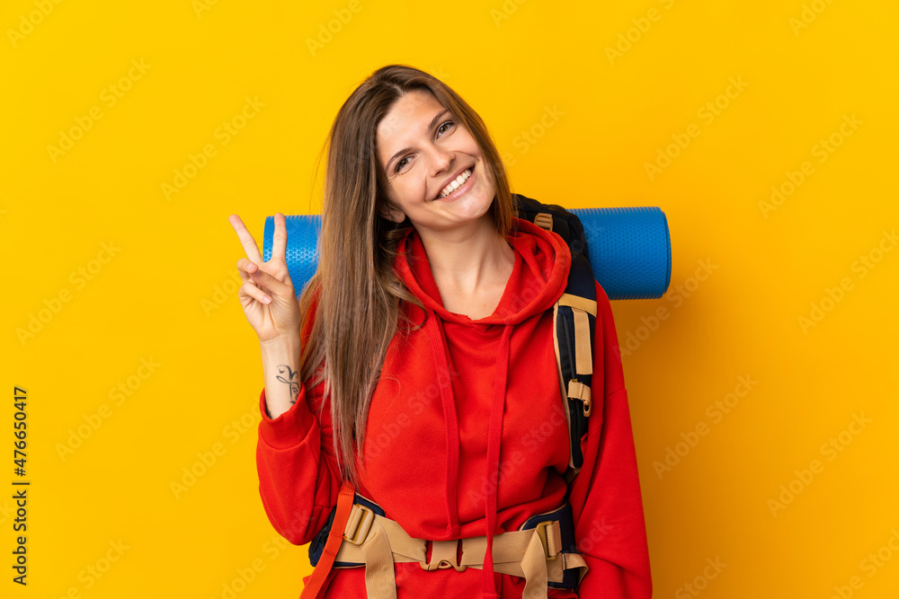Slovak mountaineer woman with a big backpack isolated on yellow background smiling and showing victory sign Slovak mountaineer woman with a big backpack isolated on yellow background smiling and showing victory sign