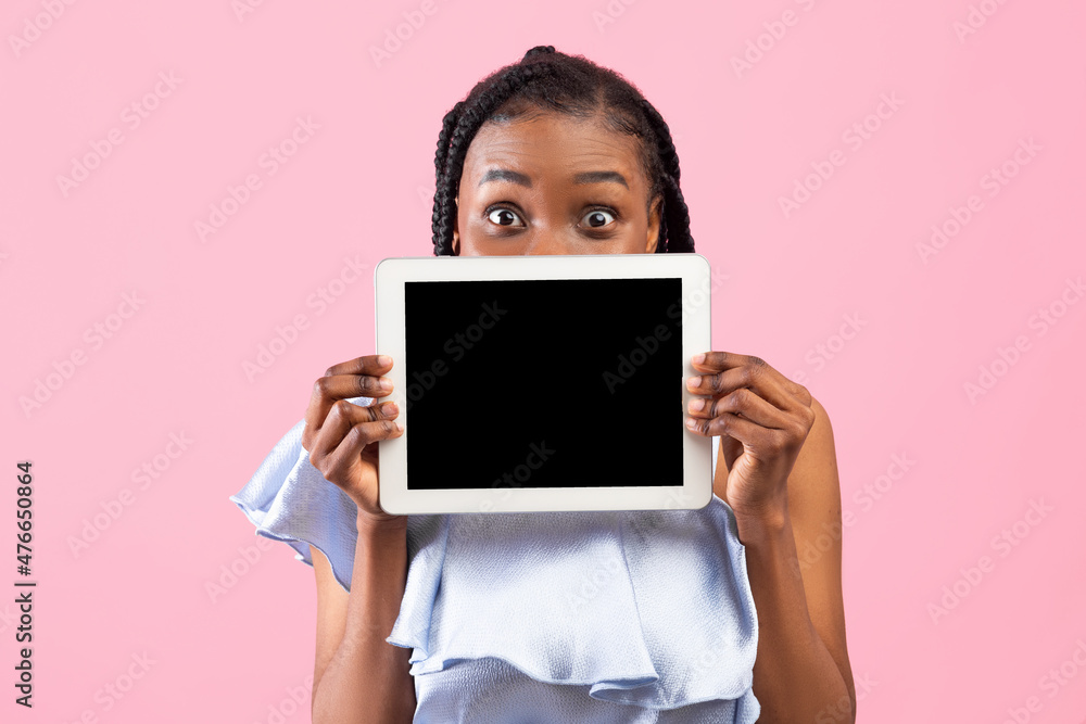Millennial black lady hiding behind tablet pc with blank screen on pink studio background, mockup for app or website Millennial black lady hiding behind tablet pc with blank screen on pink studio background, mockup for app or website