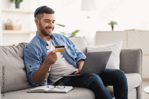 Smiling jewish guy showing credit card at home