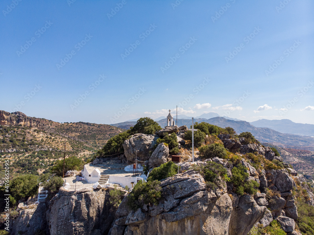 Fototapeta premium Timios Stavros Kirche auf Kreta, Griechenland, gebaut auf dem Gipfel eines kleinen Berges mit Gipfelkreuz und der Griechland Flagge