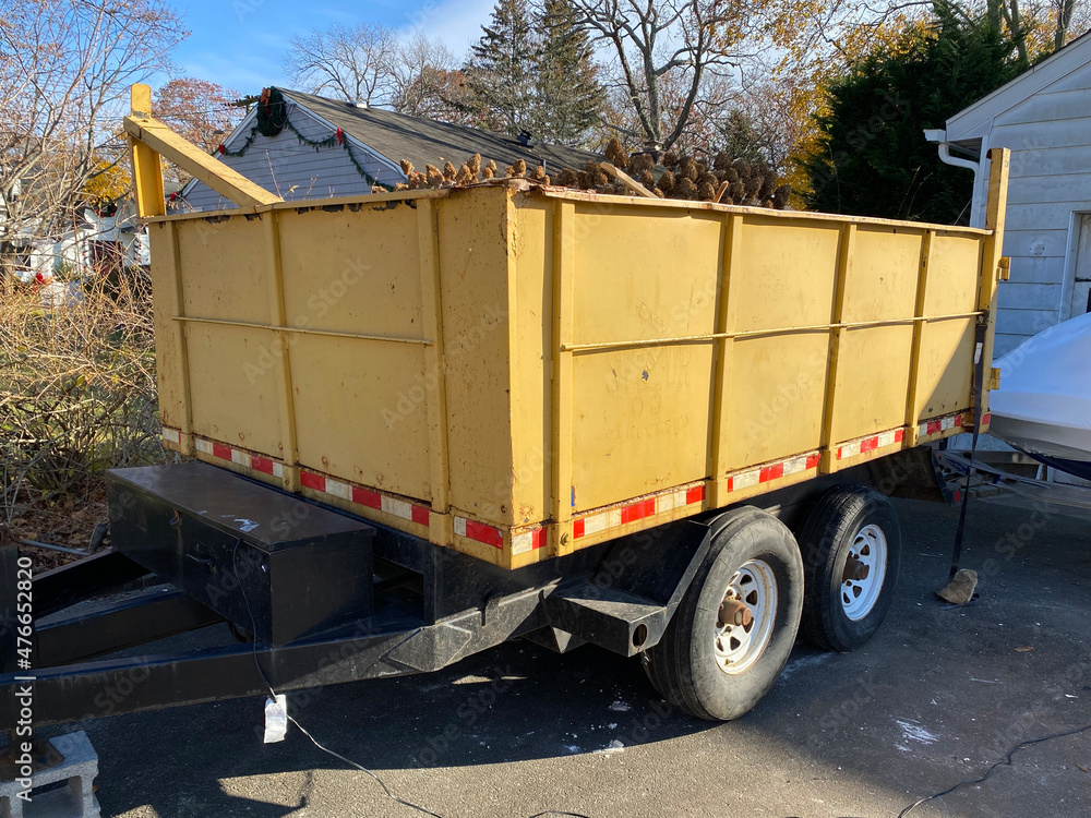 Naklejka premium Yellow dumpster on a black trailer in a homes driveway