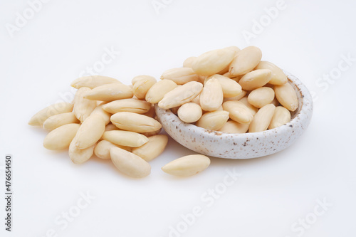 Pile of peeled or blanched almonds. White bowl of peeled whole almonds on white background. Shallow depth of field