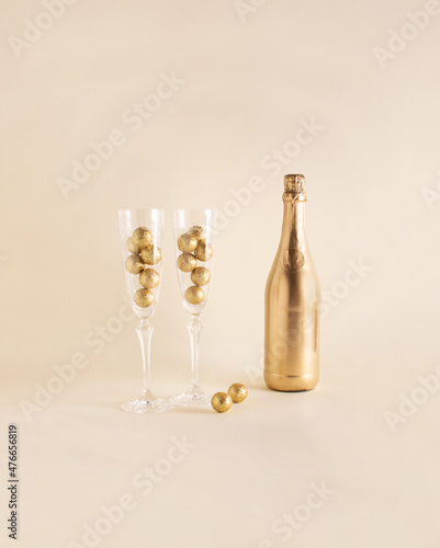 Golden bottle of champagne, two flute glasses and golden balls. Sparkling drink idea, celebration, toast for two. New Year, special event, anniversary.