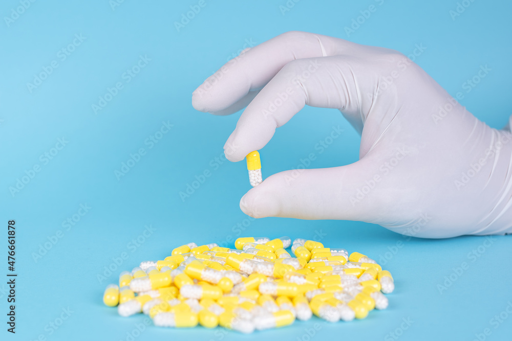 hand with surgical glove taking yellow capsules or pills with white lozenges medicine on blue background hand with surgical glove taking yellow capsules or pills with white lozenges medicine on blue background