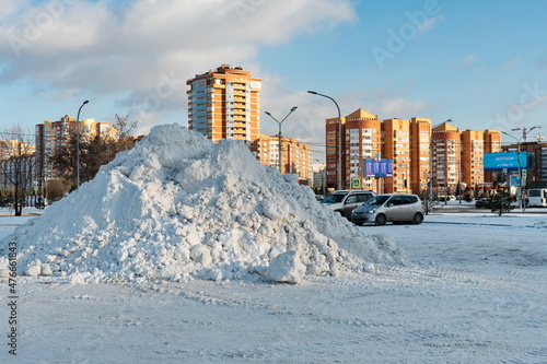 A large pile of snow lies on the street after a snowfall with residential district in the background.