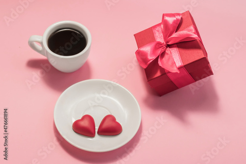 A cup of coffee, two chocolate hearts on a saucer and a gift box on a pink background. Love, birthday, engagement and Valentine's Day concept. Festive background.