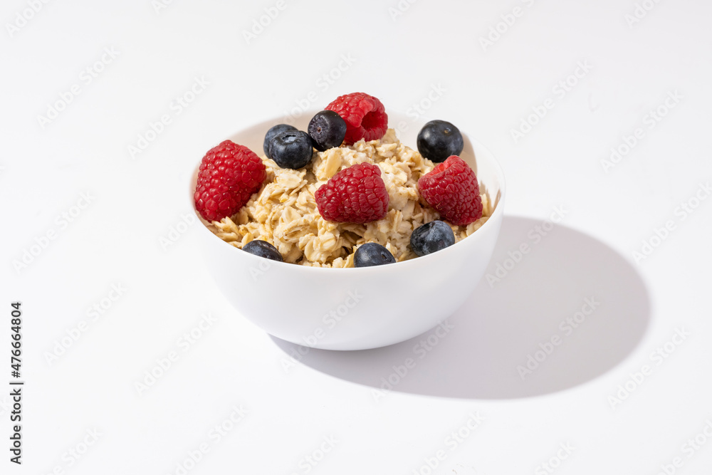 oatmeal with raspberries and blueberries in white bowl on white table. Top view. oatmeal with raspberries and blueberries in white bowl on white table. Top view.
