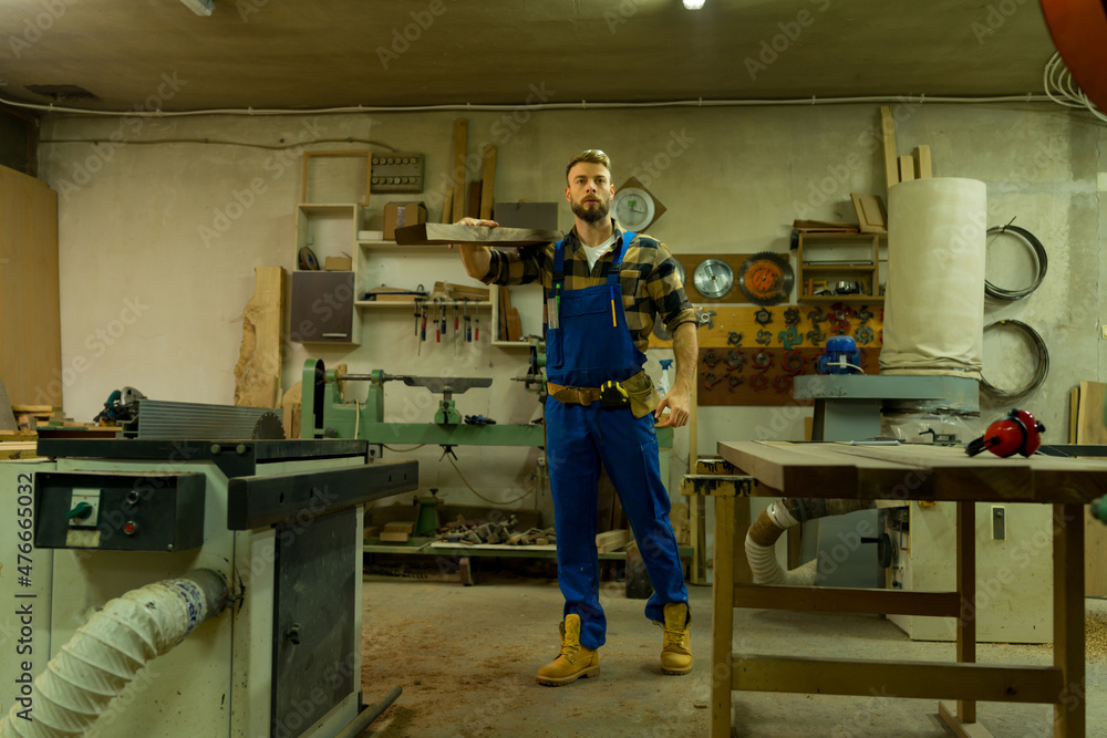 Handsome carpenter carries the long board through workshop Handsome carpenter carries the long board through workshop