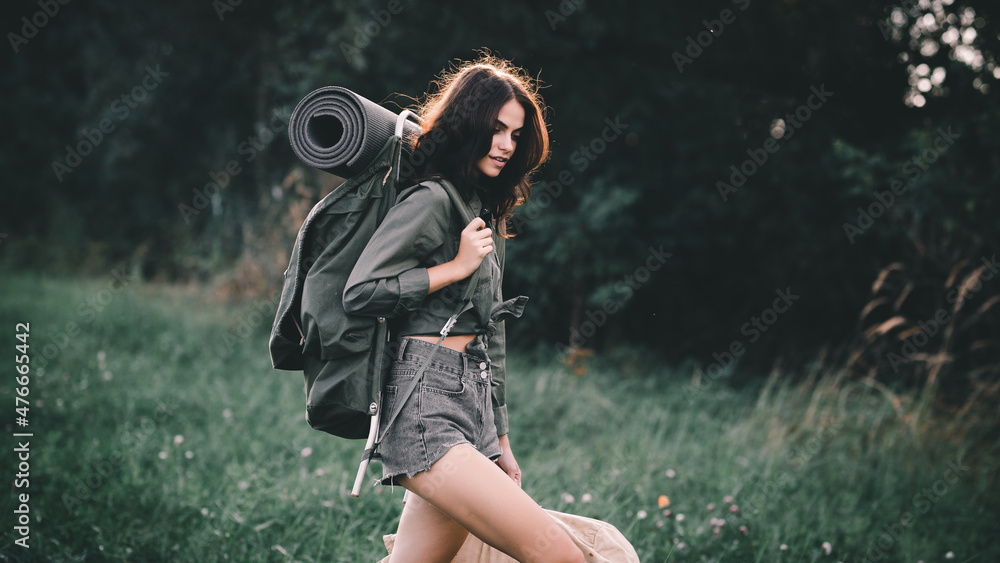 Hiking. A young girl with a retro backpack for hiking walks along a clearing road. Hitch-hiking