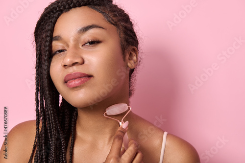 Young African American woman massaging her neck, using jade roller stone massager. Close-up