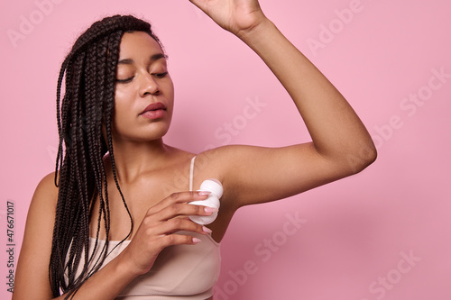 Beauty portrait. Close-up of African woman with dreadlocks in beige underwear applying antiperspirant under the armpits. Purity, hygiene, body care concept.