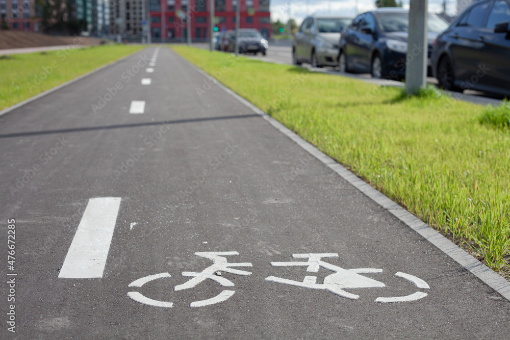 Obraz premium New empty bicycle path closeup with green grass and cars around. White bike symbol on road. Bicycle infrastructure in the city. Bikeway with no people. Separated road for cycling.