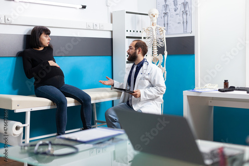 General practitioner consulting pregnant woman in cabinet, doing checkup visit to receive medical advice about pregnancy. Patient expecting child attending appointment with doctor.